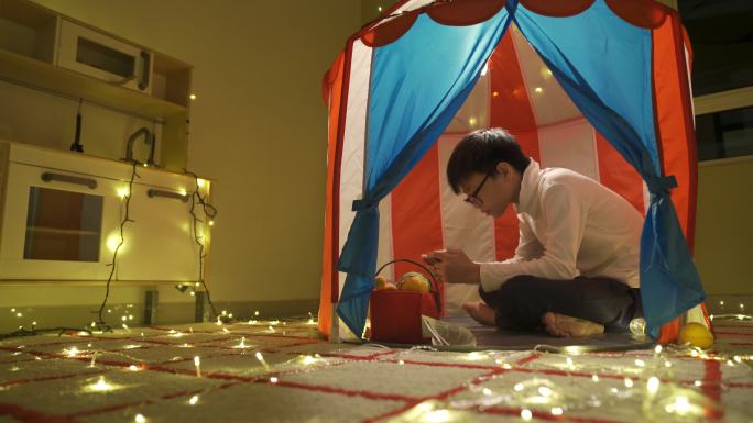 一个亚裔中国少年在家里一个舒适的照明帐篷里使用手机