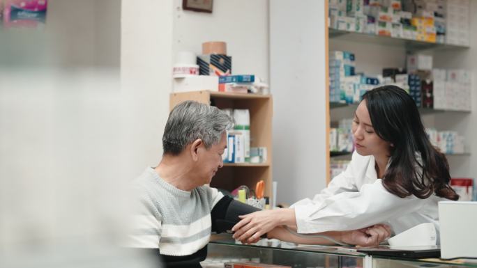 亚裔中国女药剂师在药店药房与一名资深男子一起测量血压