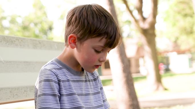 一个悲伤、沉思的小男孩坐在校园里，看着被欺负