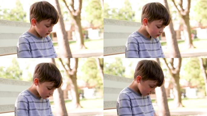 一个悲伤、沉思的小男孩坐在校园里，看着被欺负