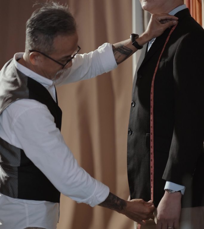 亚洲中国成熟男装裁缝，脸上留着胡茬，测量客户的身体尺寸，以制作新西装