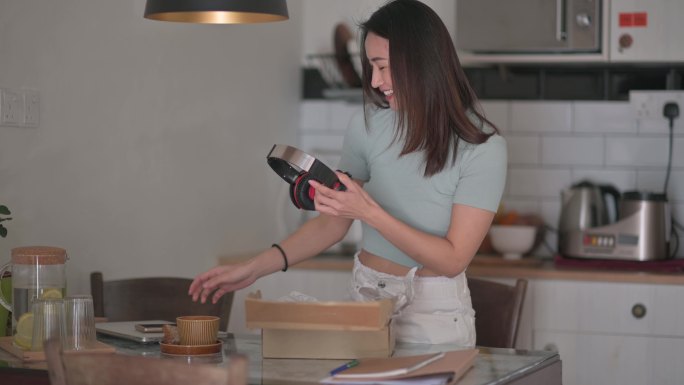 亚裔中国美女在厨房接受解包，试着从网上购物的耳机