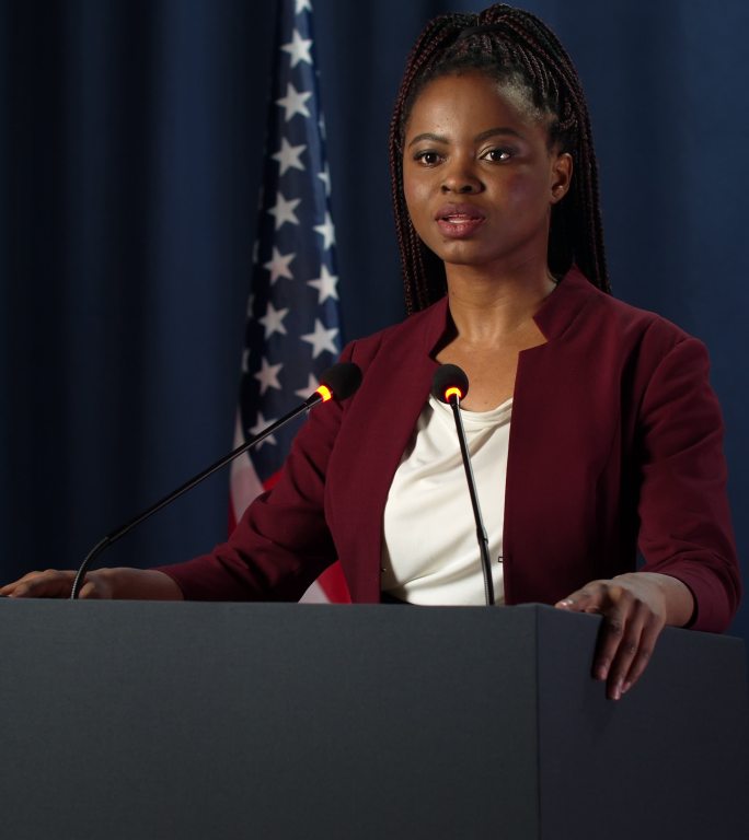 一位年轻、皮肤黝黑、自信的女政治家进入画面，在辩论中开始演讲