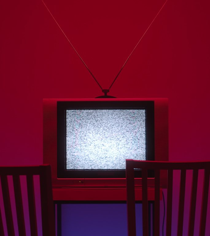 在一个黑暗的房间里，一个电视静态噪音的垂直视频在画面的中间，前面有两把椅子