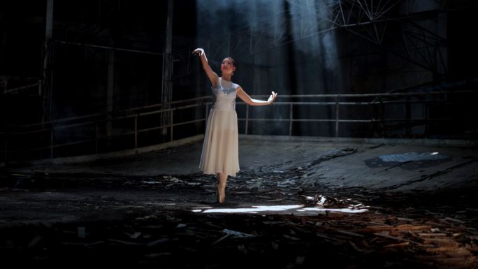年轻女子美丽的芭蕾舞演员在黑暗中随着烟雾在灯光下跳舞。