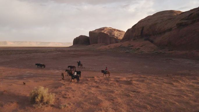 黄昏时分，在亚利桑那州的纪念碑谷部落公园里，纳瓦霍族青少年骑在马背上的无人驾驶飞机