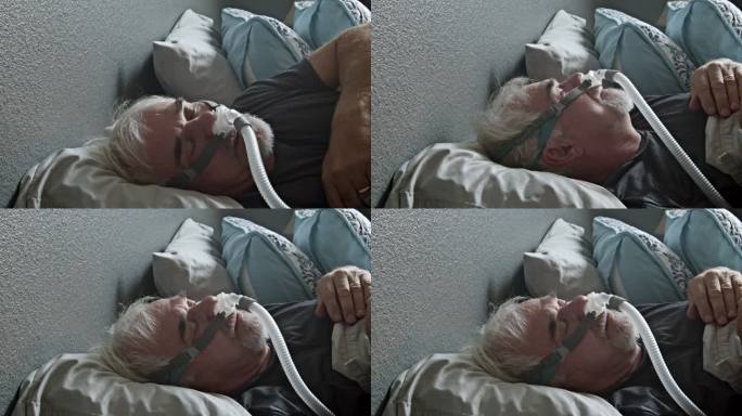 患有睡眠呼吸暂停的成年男子戴着CPAP面罩在床上睡觉