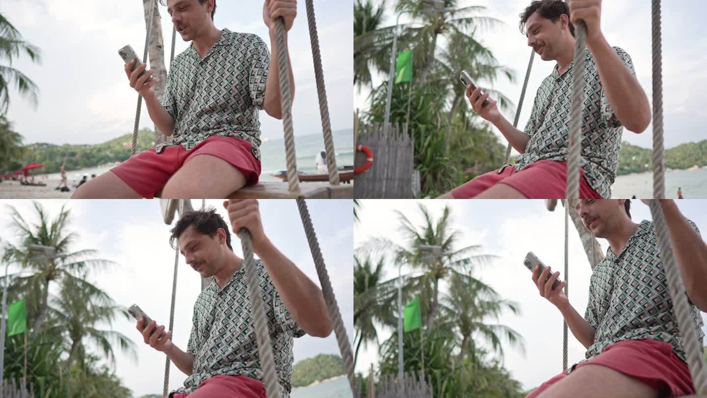 在海滩上，年轻人在荡秋千绳上荡秋千，同时通过手机进行视频通话
