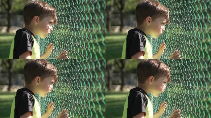 严肃、沉思的小男孩透过篱笆看