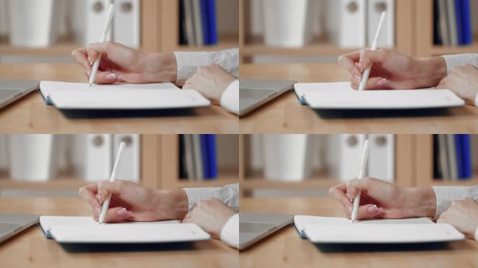 一位女商人正在用笔和笔记本电脑在记事本上写字。