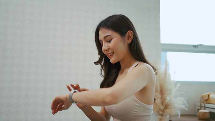 一位亚洲妇女在家里锻炼后，正在使用智能手表测量心率。