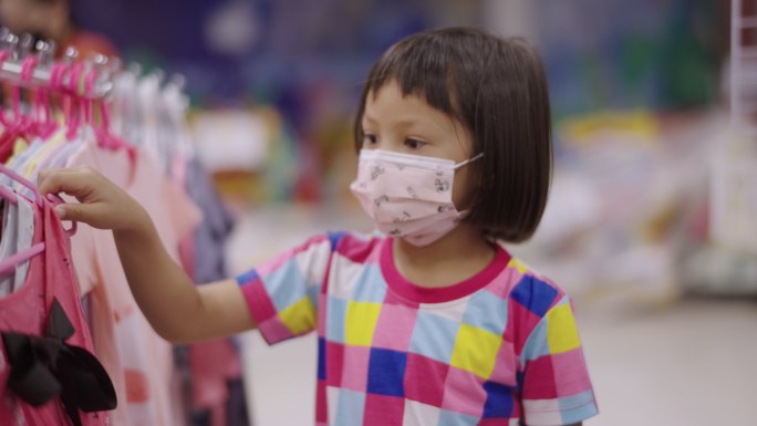 一个戴着口罩的亚洲女孩走在当地的超市里，看着货架上的产品。