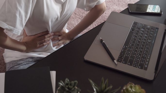 一名亚洲女性在家远程使用笔记本电脑时出现骨盆疼痛和胃痛
