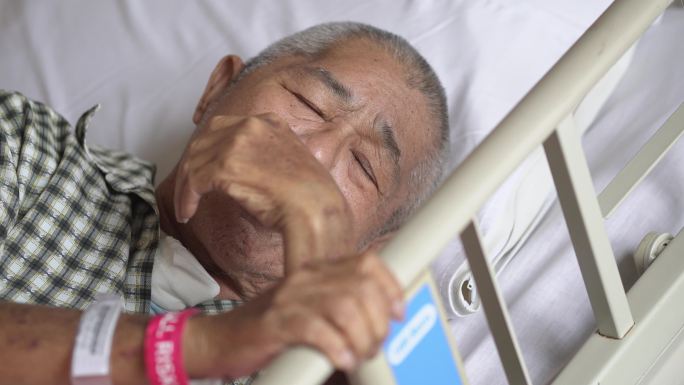 亚裔中国老年男性患者疼痛，躺在医院病房的床上休息
