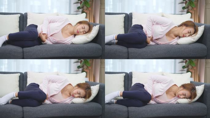 一名亚洲妇女在家中躺着或坐在沙发上胃痛，期间感到疼痛