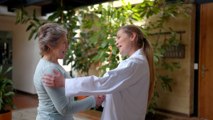 一位友善的女医生在看病后与年长的女病人握手道别