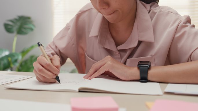 特写镜头：一位年轻的亚洲女性在办公室工作时在笔记本上写字。