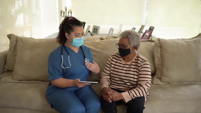 护士在家访期间使用数字平板电脑与患者交谈-佩戴防护面罩