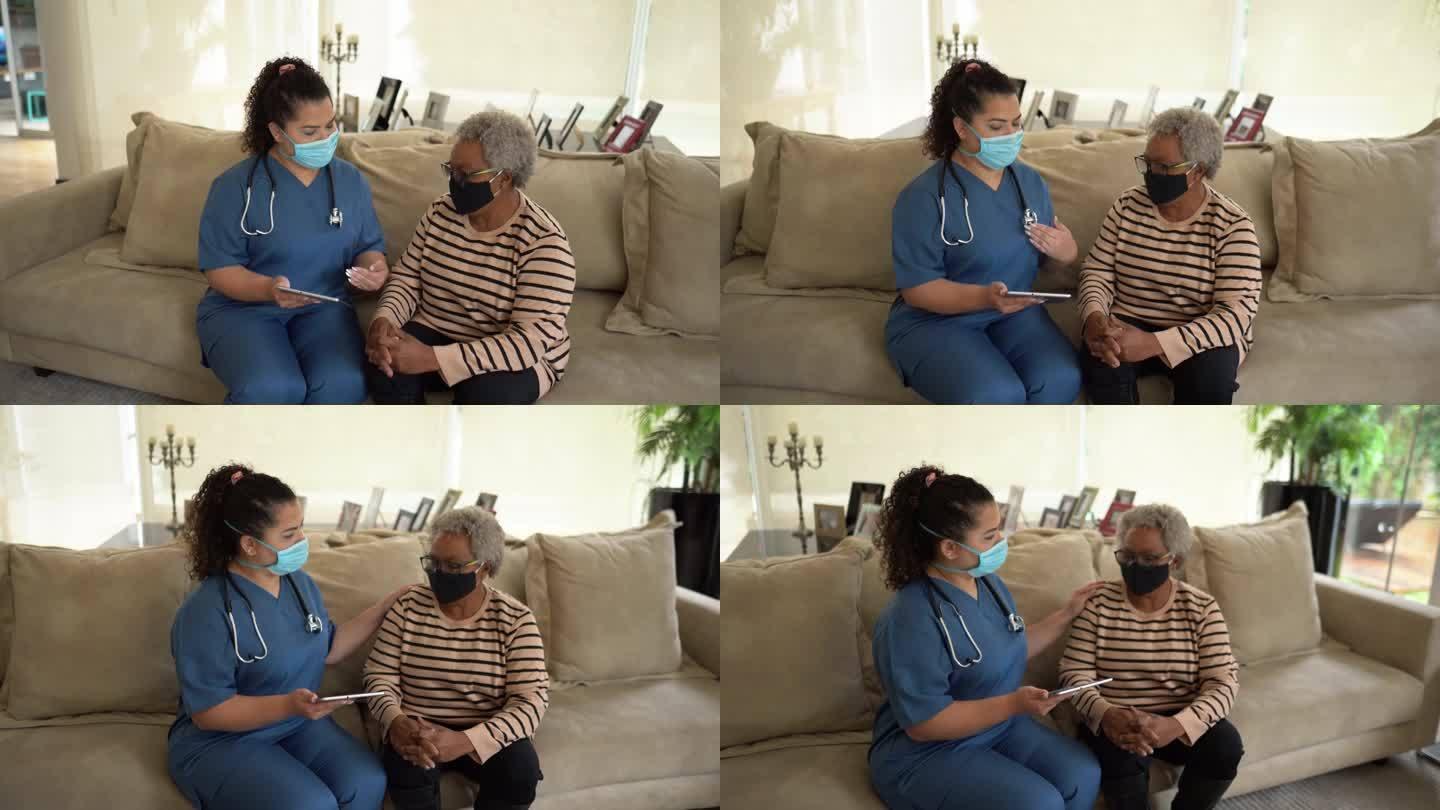 护士在家访期间使用数字平板电脑与患者交谈-佩戴防护面罩