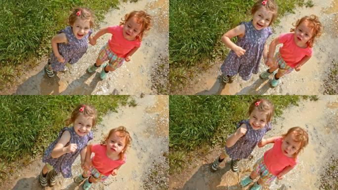 斯洛·莫：两个小女孩手牵着手在水坑里跳跃，对着镜头微笑