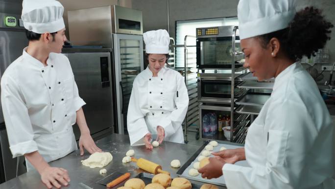 穿着白色制服的快乐的多种族青年厨师们一起工作，制作面包、面包和法式面包，在烤箱中打样和烘烤之前进行一