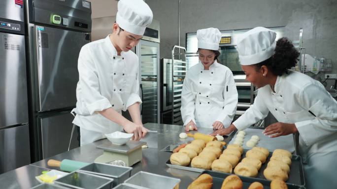 穿着白色制服的多种族青年厨师一起工作，制作面包、面包和法式面包，在烤箱中打样和烘焙之前称重、揉捏和成