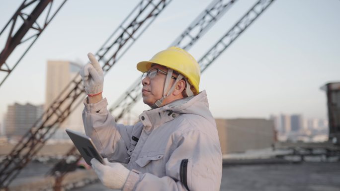 亚洲高级工程师在屋顶操作笔记本电脑，夕阳照在头盔上