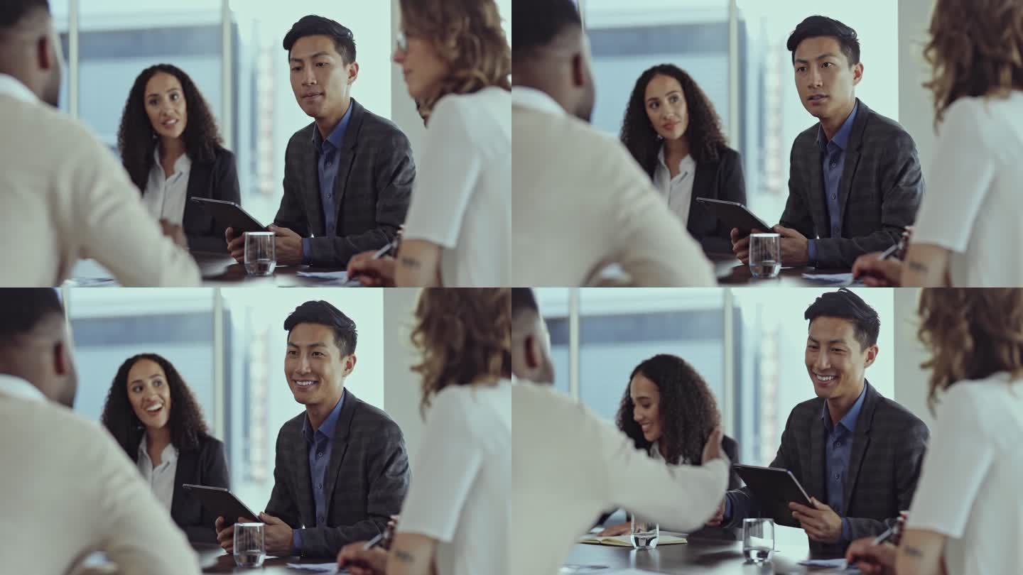 一位年轻的亚洲商人坐在会议室的一张桌子上，与同事交谈并握手。两位商人在工作面试中交谈并握手