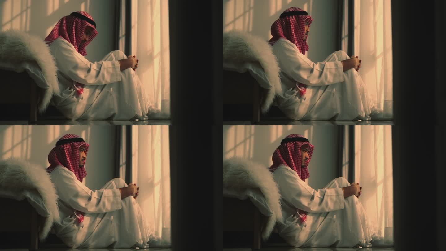 一位年轻的阿拉伯男子坐在卧室的地板上，带着沮丧的表情蹲在地上。
