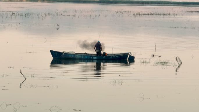 一个农民男子在湖面上钓鱼反映在晨曦中，一个人靠钓鱼谋生，一个人独自在湖心钓鱼，钓鱼是一种爱好