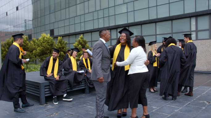 毕业典礼结束后，快乐的黑人家长走向女儿，祝贺她与同学们交谈