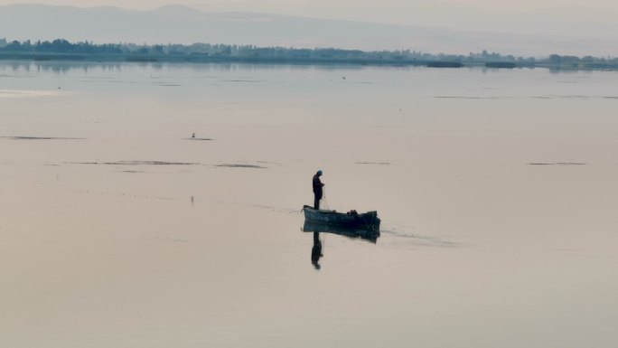 一个农民男子在湖面上钓鱼反映在晨曦中，一个人靠钓鱼谋生，一个人独自在湖心钓鱼，钓鱼是一种爱好