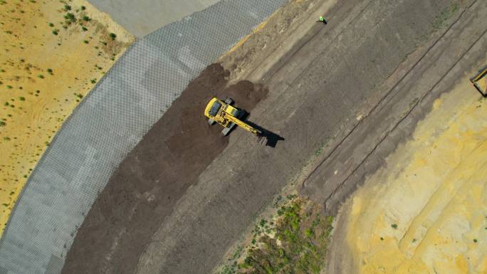 带有连续履带的黄色挖掘机。鸟瞰图。向下移动相机并放大。施工现场准备。卡车和工人可见。不同土层。