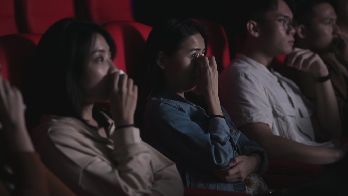 亚裔中国女性在电影院电影院看悲伤感伤的戏剧电影时哭着用纸巾擦眼泪