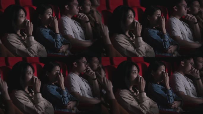 亚裔中国女性在电影院电影院看悲伤感伤的戏剧电影时哭着用纸巾擦眼泪