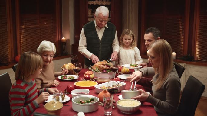 孙女在感恩节晚餐上等爷爷给她切火鸡片
