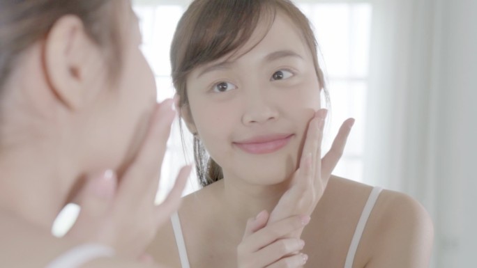 美丽的亚洲年轻女性乐于在面部涂抹润肤霜或润肤乳，美丽的亚洲女孩使用护肤品来接触面部化妆，健康和健康理