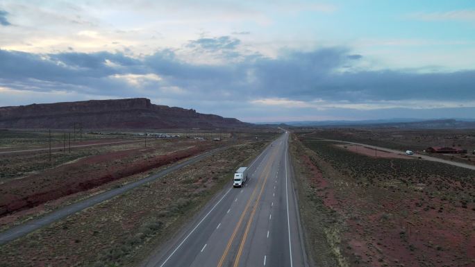无人机视图半卡车在犹他州西南部摩押附近的红岩砂岩地区沙漠中沿四车道公路加速行驶
