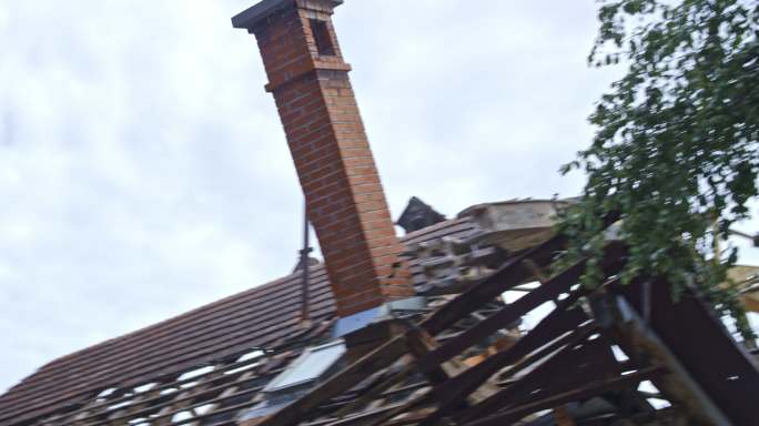 砖烟囱被挖掘机推下正在拆除的房屋屋顶