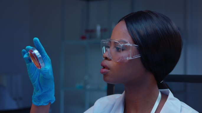 一位年轻的非洲裔美国女性微生物学家正在观察皮氏培养皿上的医学细菌检测结果