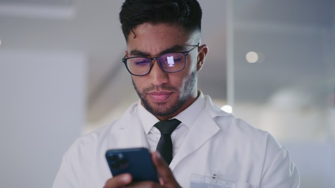 一位科学家在实验室内用手机打字的特写镜头，一位西班牙裔男性技师正在用手机微笑。Happy covid