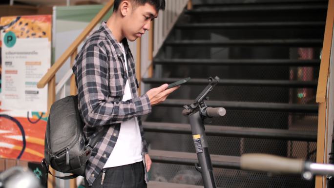 年轻人手持智能手机在车站解锁电动滑板车