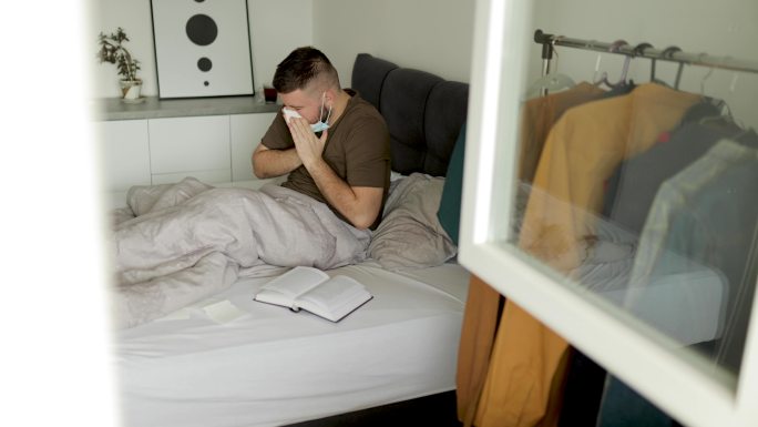 一张年轻男子生病并在床上用纸巾擤鼻子的照片