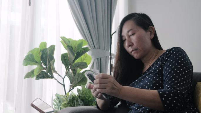亚洲成年女性坐在家里靠窗的沙发上，检查血压后，准备服用抗高血压药，这是一种生活方式理念。