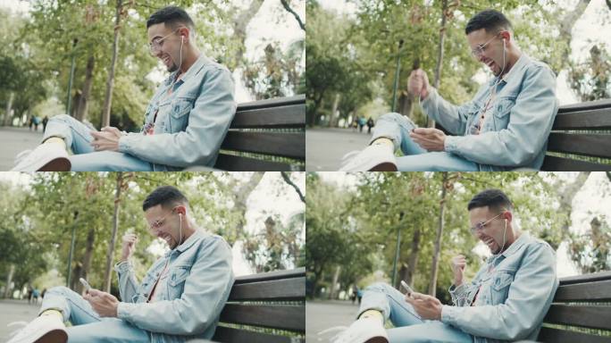 一个年轻人在公园的长凳上放松时，用带耳机的智能手机庆祝的4k视频片段