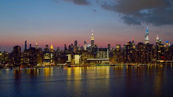 日落时分，纽约市曼哈顿中城东河对岸的远处全景夜景。具有平移转发运动的空中视频。