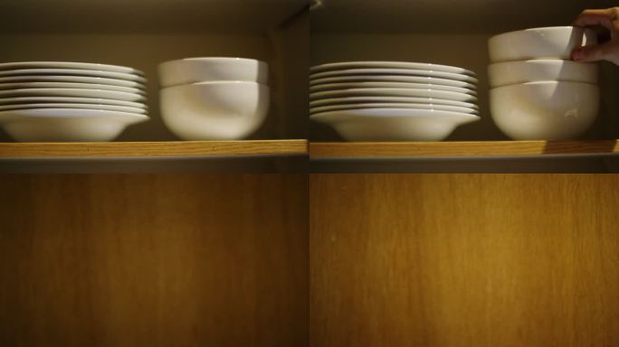 一位白人女性的手将各种尺寸的干净碗放入开放式厨房橱柜，然后关上门