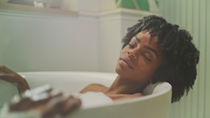 美丽的非洲裔女性在现代浴室里放松。佩戴保湿凝胶眼罩和冥想