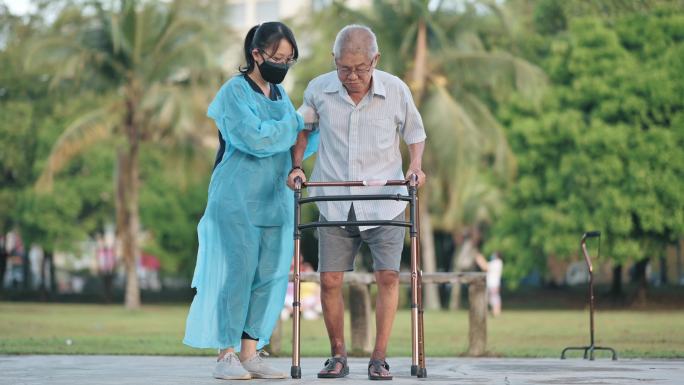 亚裔华人女性理疗师用助行器矫正姿势帮助老年男子在公园行走