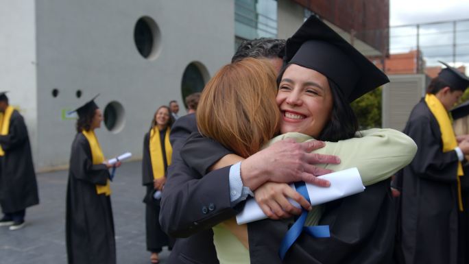 快乐的研究生在毕业日拥抱父母，看起来很兴奋
